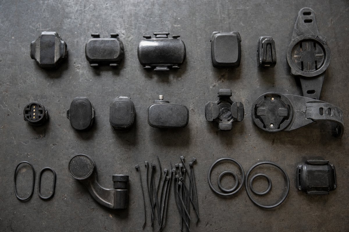 Obsolete cycling computers, sensors, mounts and cable ties laid out in rows on a grey concrete surface (AI-generated image)